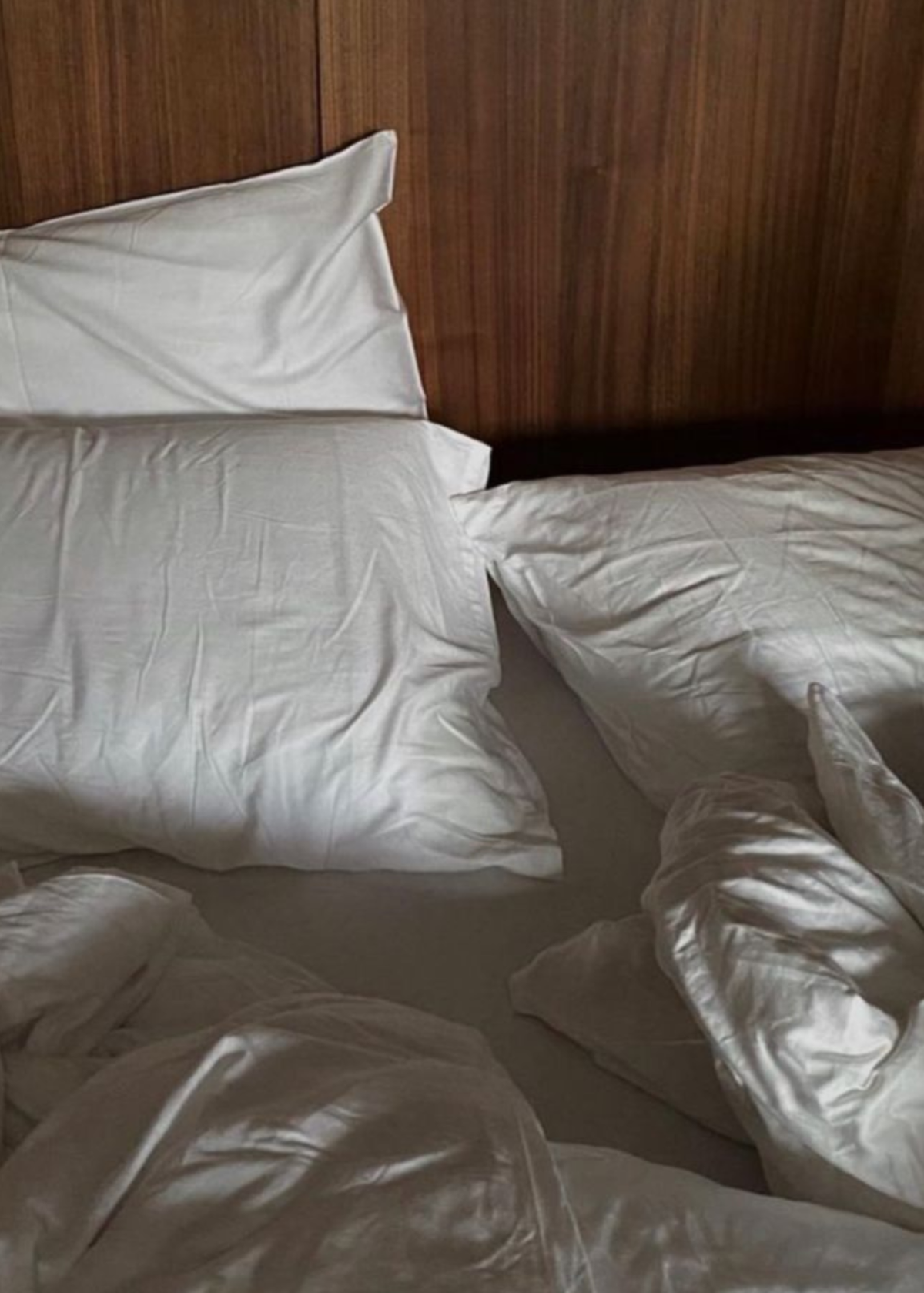 White bedding with two pillows and rumpled duvet on a bed against a dark wood headboard for The Candle Cluub's Retreat Cluub