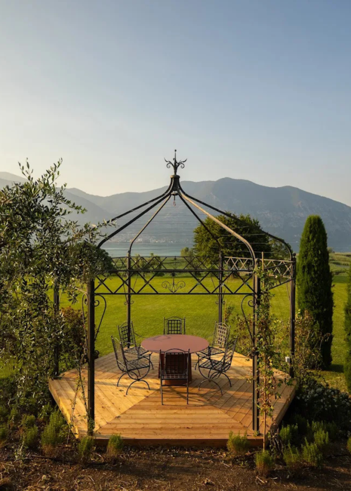 A black wrought-iron gazebo with a wooden deck and dining table - a communal space at The Candle Cluub's Retreat Cluub