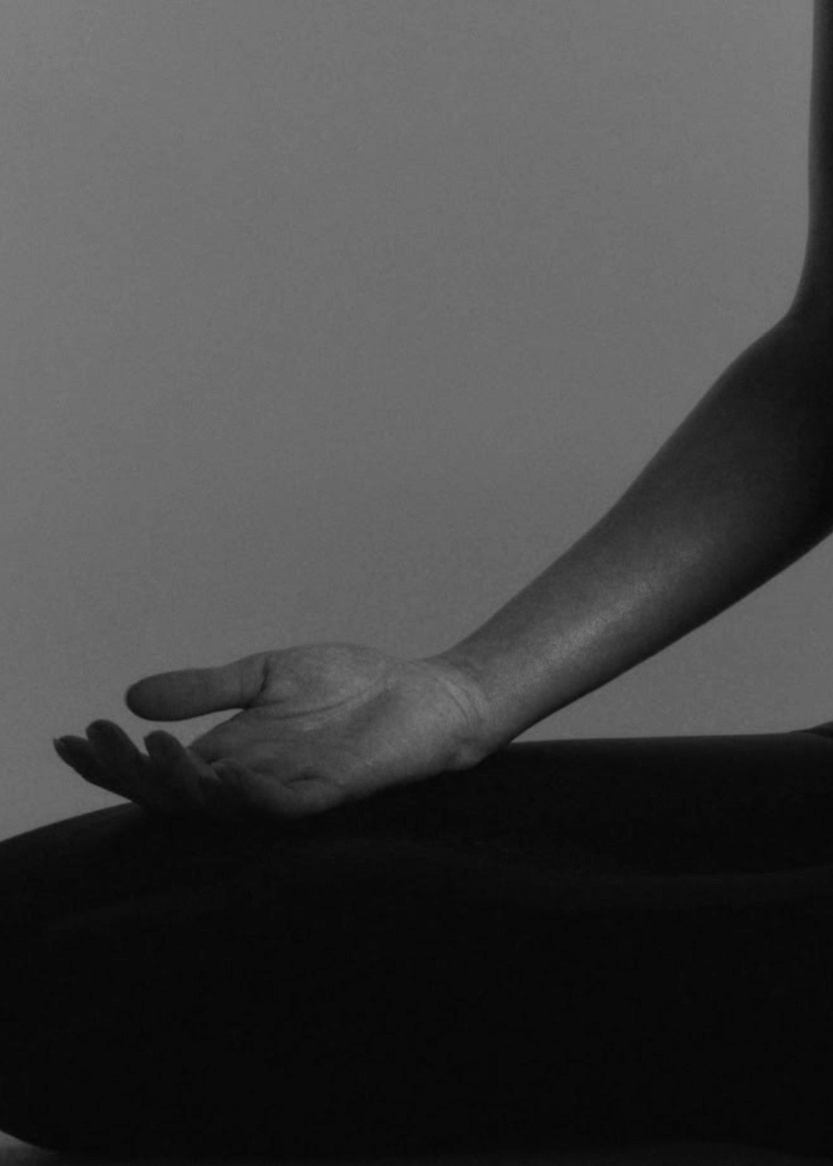 A black and white photograph of a person's arm resting on their knee in a meditative pose for The Candle Cluub Face Yoga Ritual special event