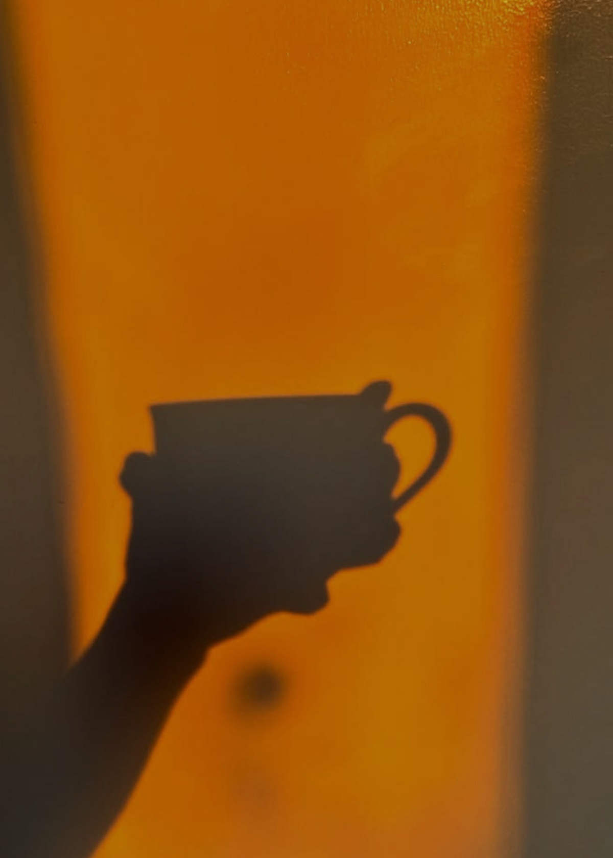 A dark silhouette of a hand holding a teacup against a warm glowing orange background for The Candle Cluub Face Yoga and Self Care Ritual Event