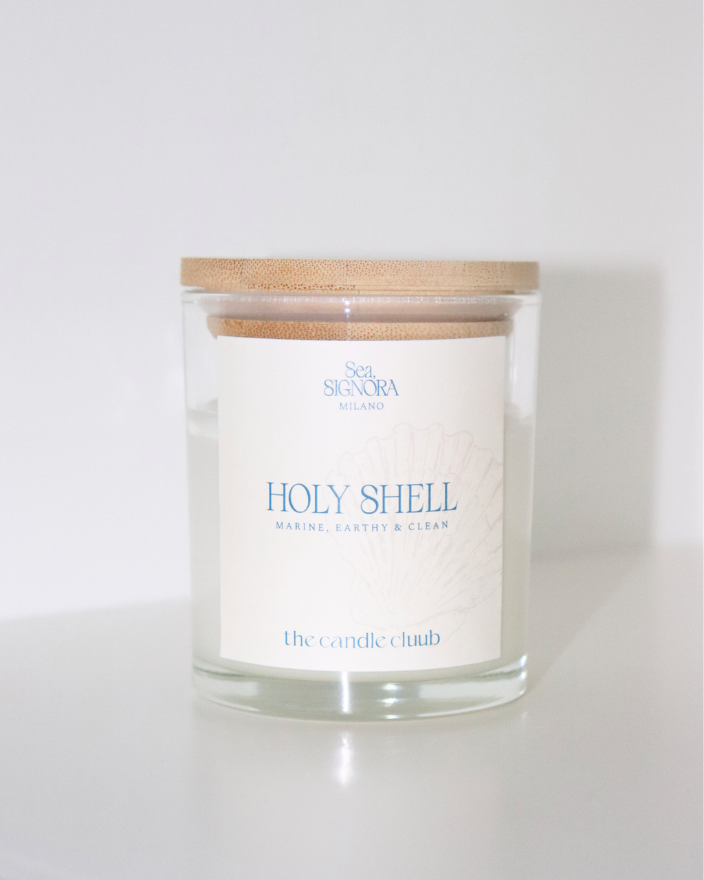 A Candle Cluub candle with a light wood lid and a white label reading 'Holy Shell' and 'the candle club', photographed on a clean white background.