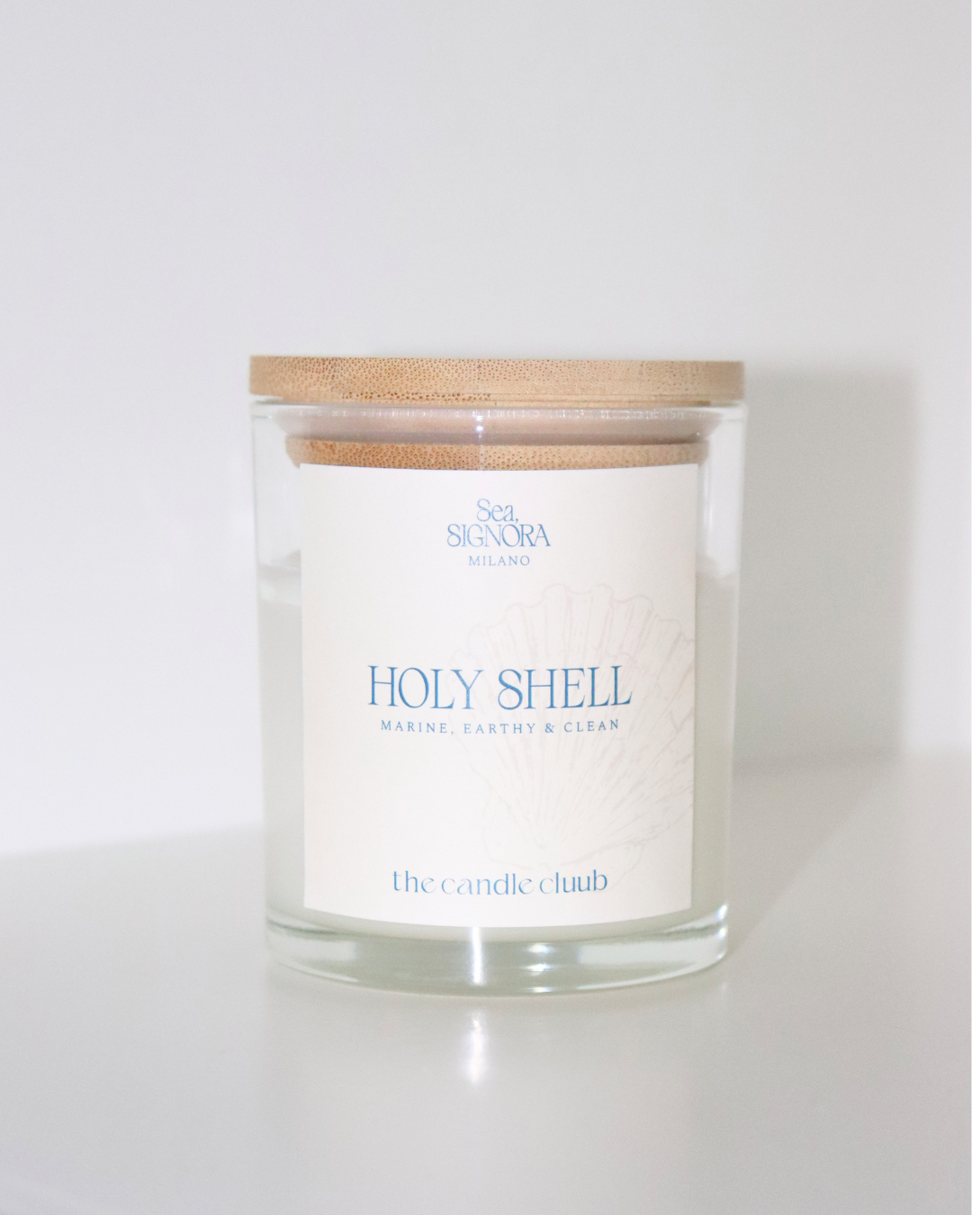 A Candle Cluub candle with a light wood lid and a white label reading 'Holy Shell' and 'the candle club', photographed on a clean white background.