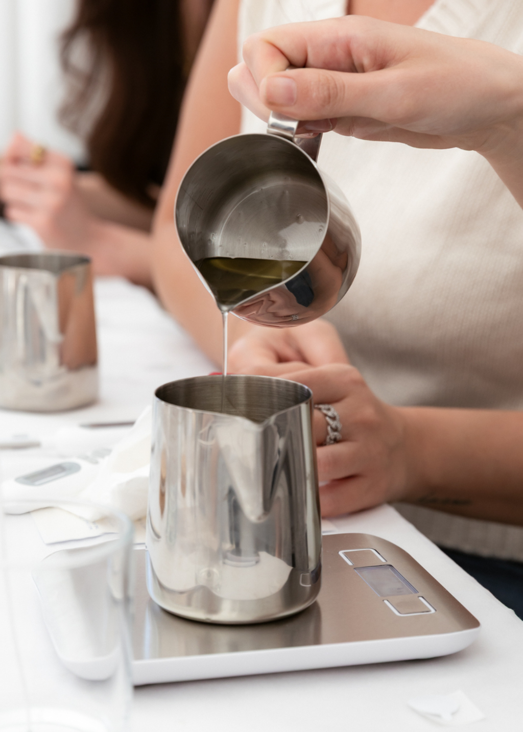 A close-up of a person pouring melted wax from a stainless steel pitcher at The Candle Cluub workshop